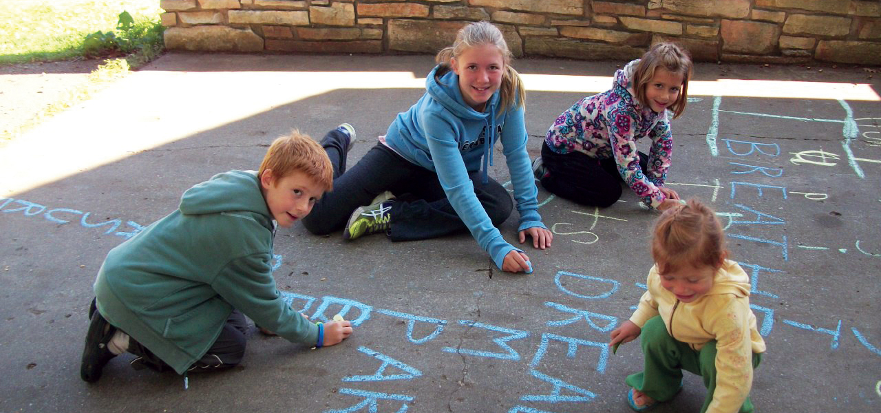 Homeschool children write spelling words in chalk on sidewalk