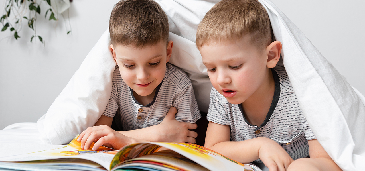 Two brothers reading picture book under a blanket