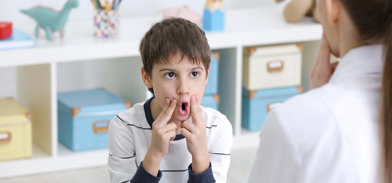 Boy practices making sounds with speech therapist